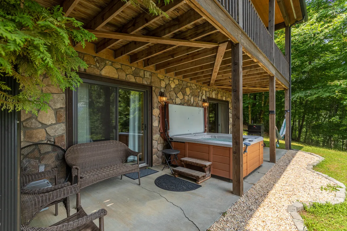 This image showcases a tranquil outdoor hot tub with a stone wall backdrop and comfortable seating, set against a natural, green environment. The arrangement highlights the inviting relaxation space and the seamless connection between indoor and outdoor living.