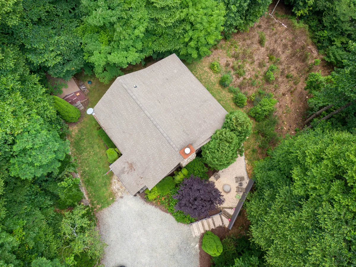 The exterior of the home with a clear view of the gravel driveway, surrounded by mature trees and a patio area. The private setting is evident, and the driveway is visible, suggesting where security measures like the camera are implemented for guests' peace of mind.
