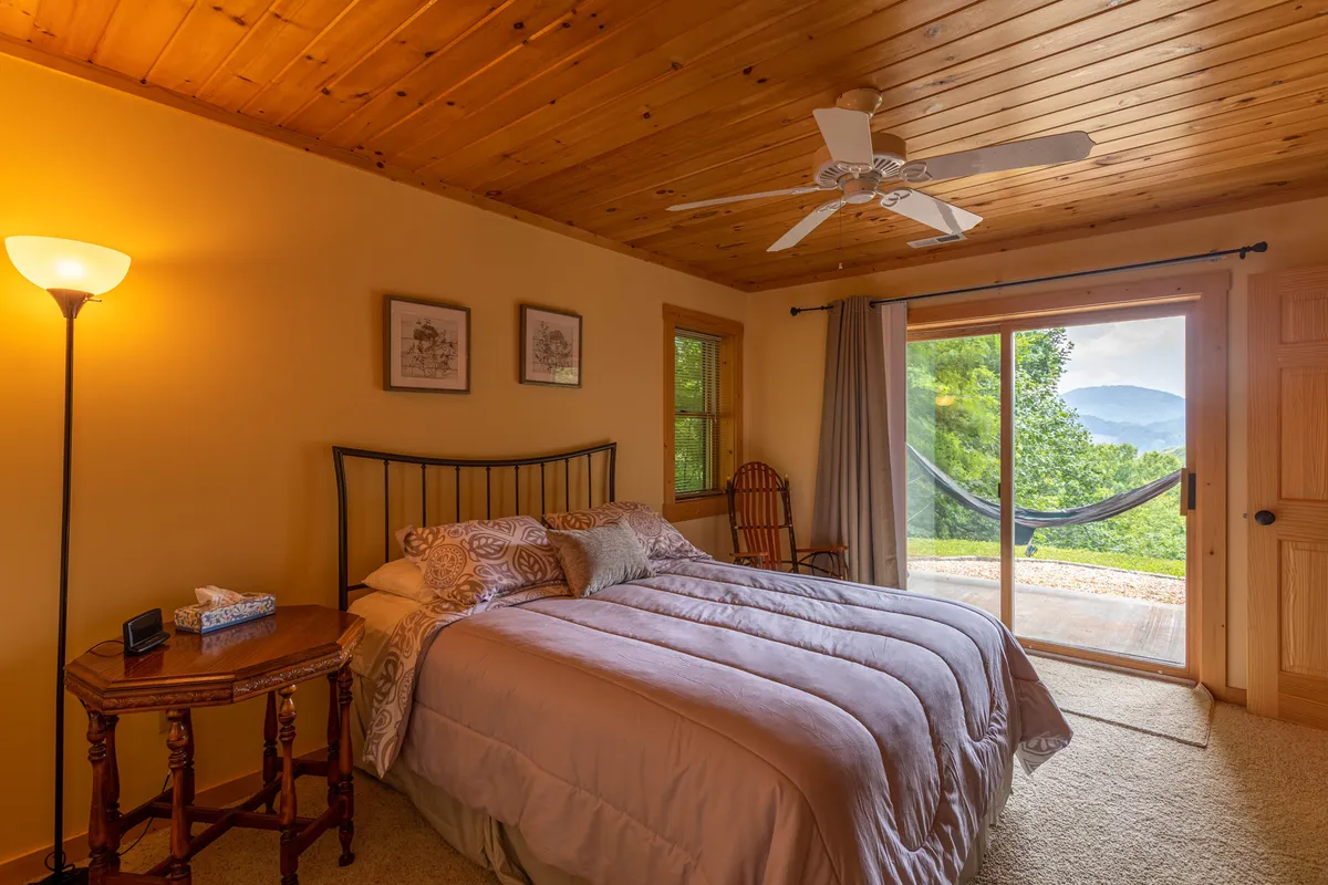 A serene bedroom with a large bed, sliding glass door opening onto the deck, and inviting decor. The scene hints at the easy transition from indoor comfort to outdoor dining or morning coffee with a view.