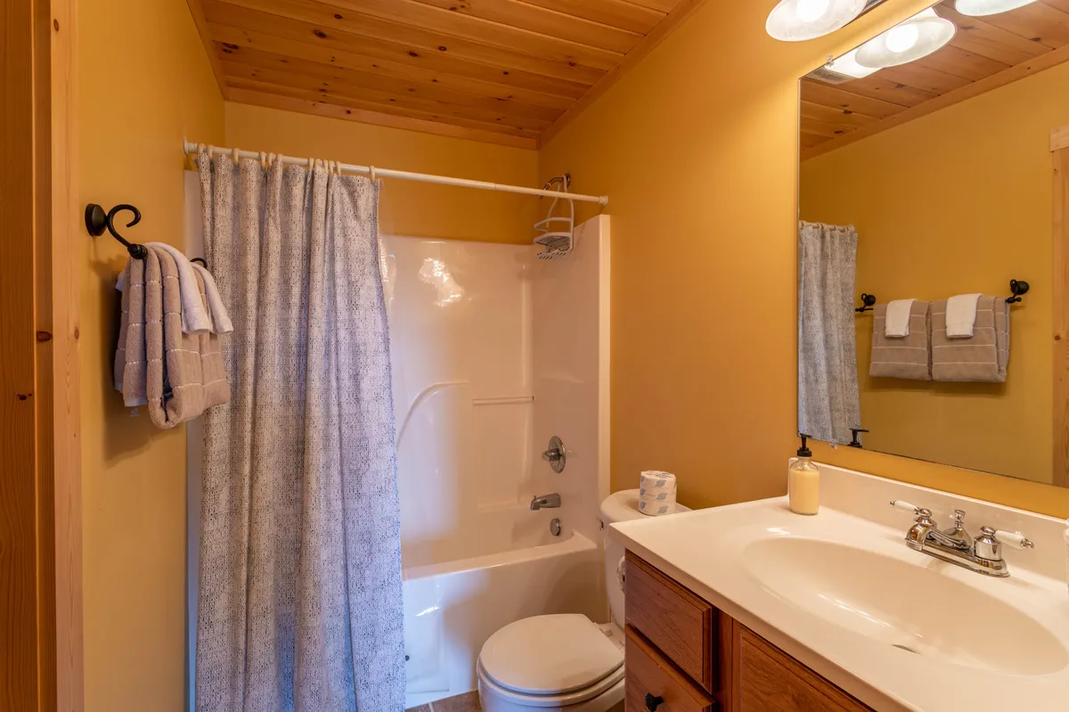 A serene bathroom with a bathtub, sink, wooden cabinetry, shower curtain, and mirror. The mood is calm and spa-like, ideal for relaxation and personal care routines after a busy day.