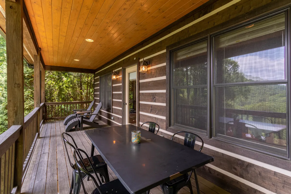 An exterior shot of the upper wooden deck, featuring a dining table and seating area overlooking tranquil natural surroundings. The deck offers an inviting space for outdoor dining and social gatherings, seamlessly connected to the interior via sliding doors.