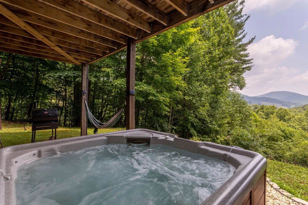 An exterior shot highlighting a hot tub, hammock, grill, and sweeping mountain views. The setting evokes relaxation and fun, with amenities for both unwinding and outdoor dining—all framed by the grandeur of the surrounding landscape.