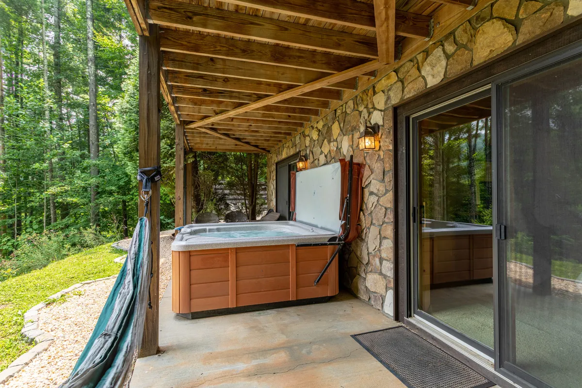 This exterior image captures a tranquil hot tub set against a stone wall with wooden beams, immersed in surrounding greenery. The setting offers a sense of privacy, relaxation, and a direct connection to nature, with enough space for couples or a small group to unwind.